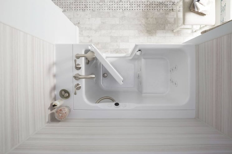 Aerial shot of an empty walk in tub that has the door open. You can see features like a walk in tub grab bar and a walk in tub seat